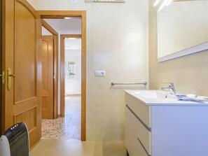 Un baño con puerta de madera, lavamanos blanco y espejo.