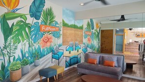 Una habitación moderna con un mural de plantas tropicales, un sofá, una mesa de centro y un escritorio con sillas.