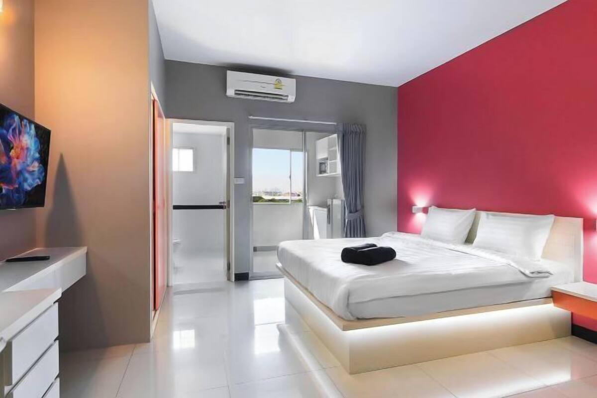 Ein modernes Hotelzimmer mit Bett, Nachttisch und Blick durch eine offene Tür auf einen Balkon.