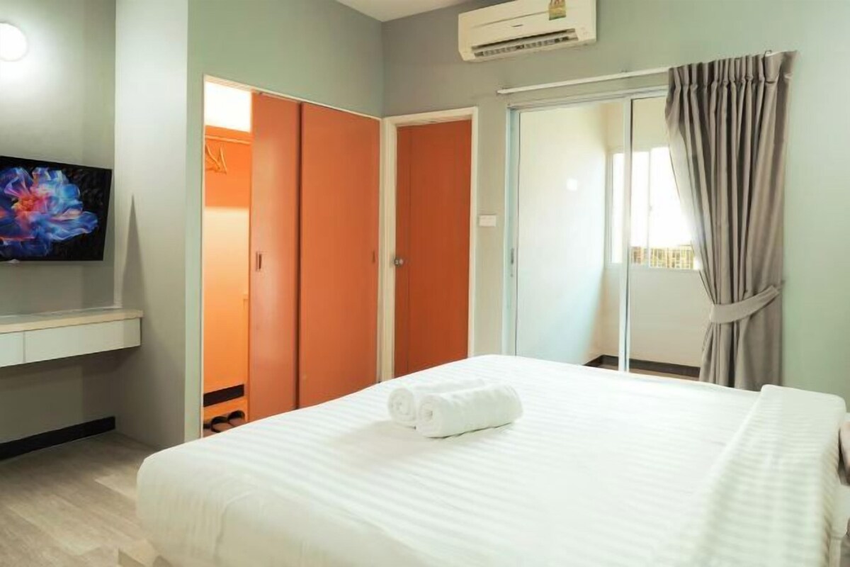 Une chambre d’hôtel équipée d’un lit, d’un téléviseur fixé au mur, d’une armoire et d’une porte-fenêtre coulissante donnant sur un balcon.