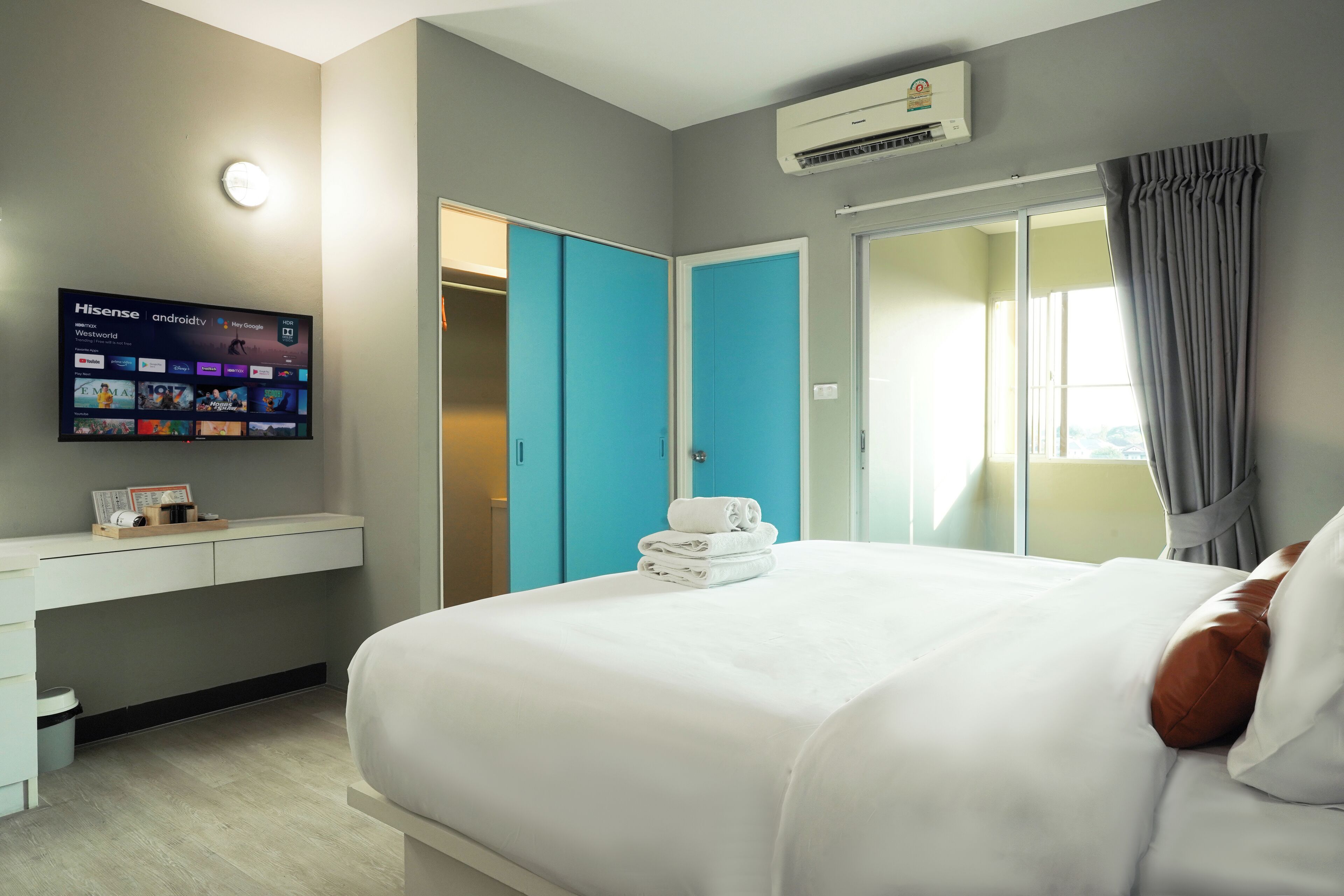 A hotel room with a bed, a TV mounted on the wall, a desk, and a closet.