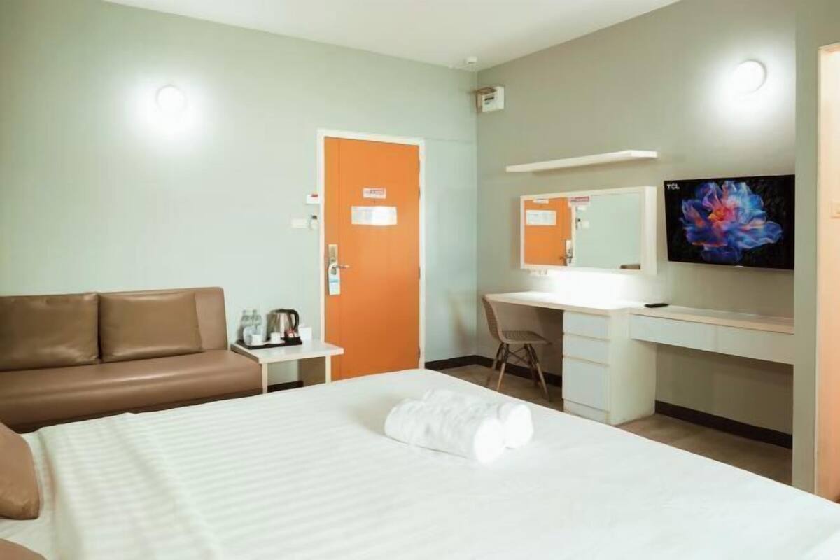 Ein Hotelzimmer mit einem Bett, einem braunen Sofa, einem Schreibtisch mit Stuhl, einem Fernseher und einer Tür.