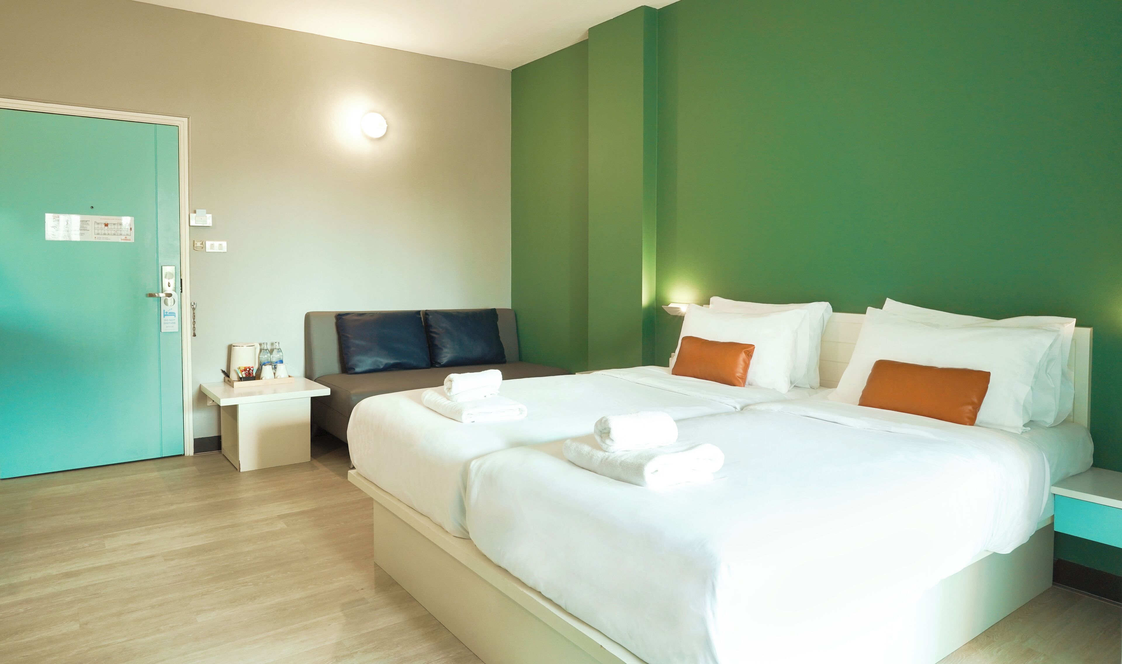 A hotel room with a large bed, a bedside table, a nightstand, and a green accent wall.