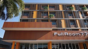 Un hotel con fachada moderna, balcones con plantas y un llamativo letrero 'FullRoom77'.