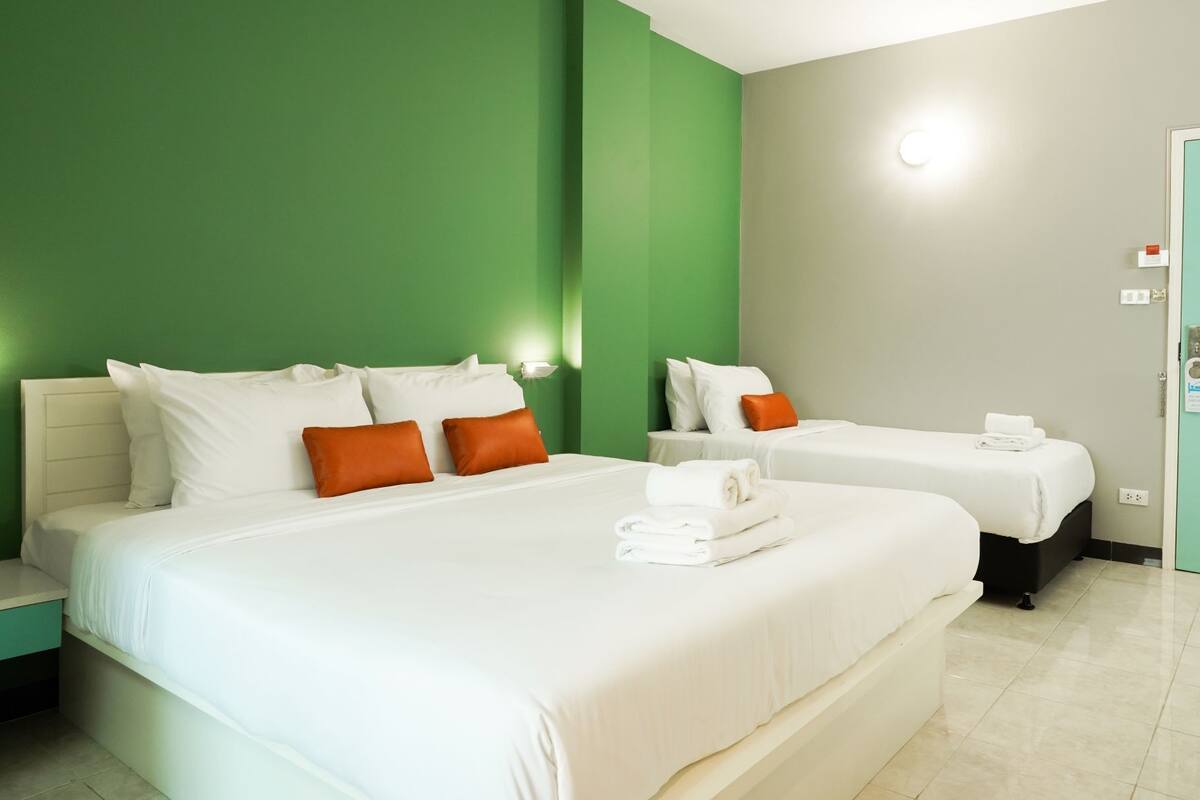 Ein Hotelzimmer mit einem großen Bett, zwei Einzelbetten, grünen Wänden, einem Lichtschalter und einer Tür.