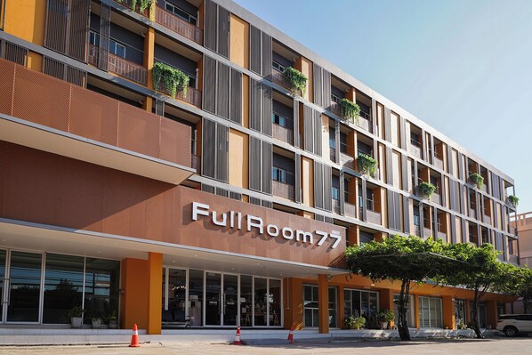 Un hotel a più piani con un evidente cartello 'FullRoom77', ampie finestre e balconi con piante.