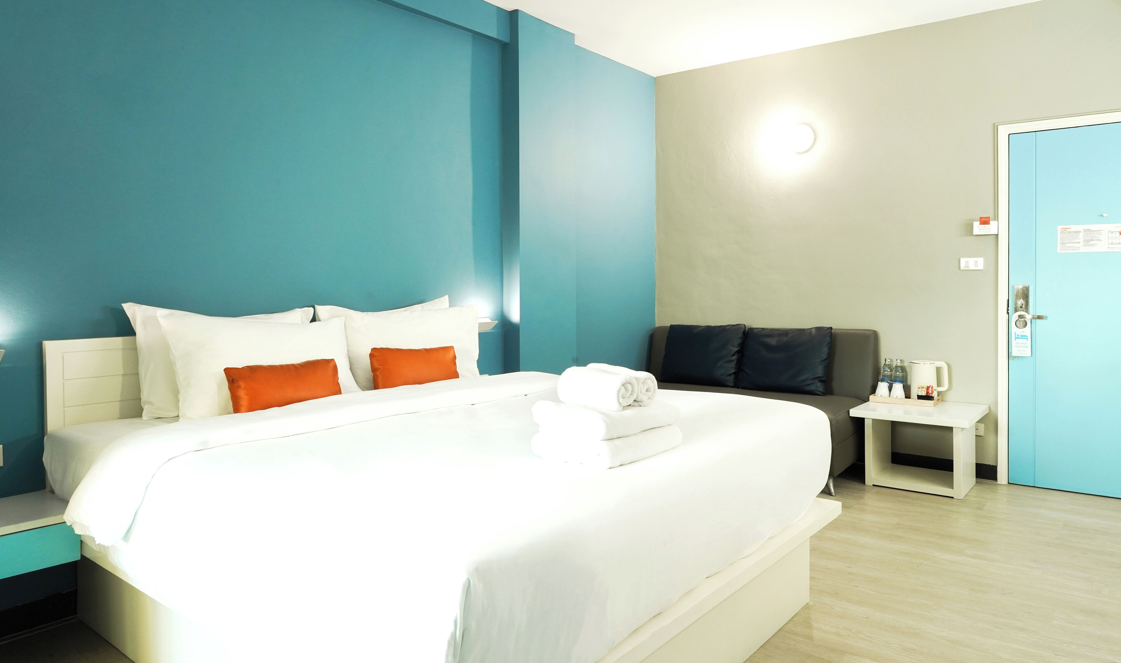 Ein Hotelzimmer mit einem großen Bett, einem Nachttisch, einem kleinen Tisch mit einer Kaffeemaschine und einer Tür mit einem Schild.