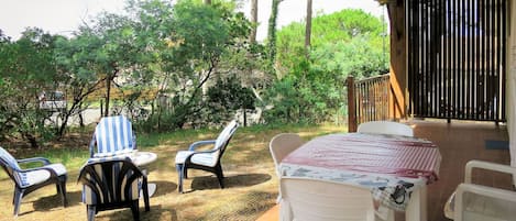 Um pátio externo com mesa e cadeiras, cercado por árvores e um muro de madeira.