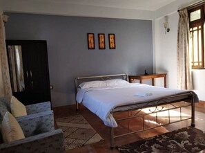 A bedroom with a metal bed frame, a bedside table, a patterned rug, and a wall with three framed artworks.