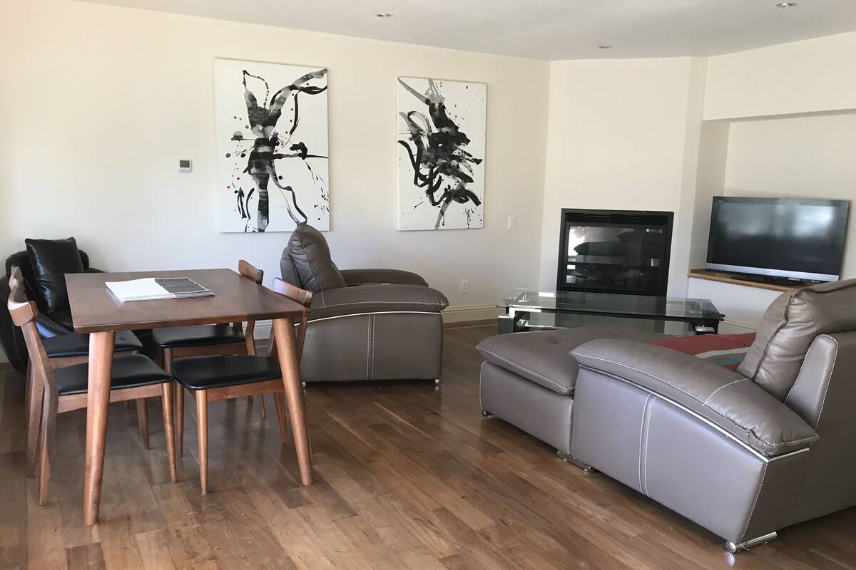 Un salon moderne avec une table à manger en bois, un canapé en cuir gris et un téléviseur à écran plat.