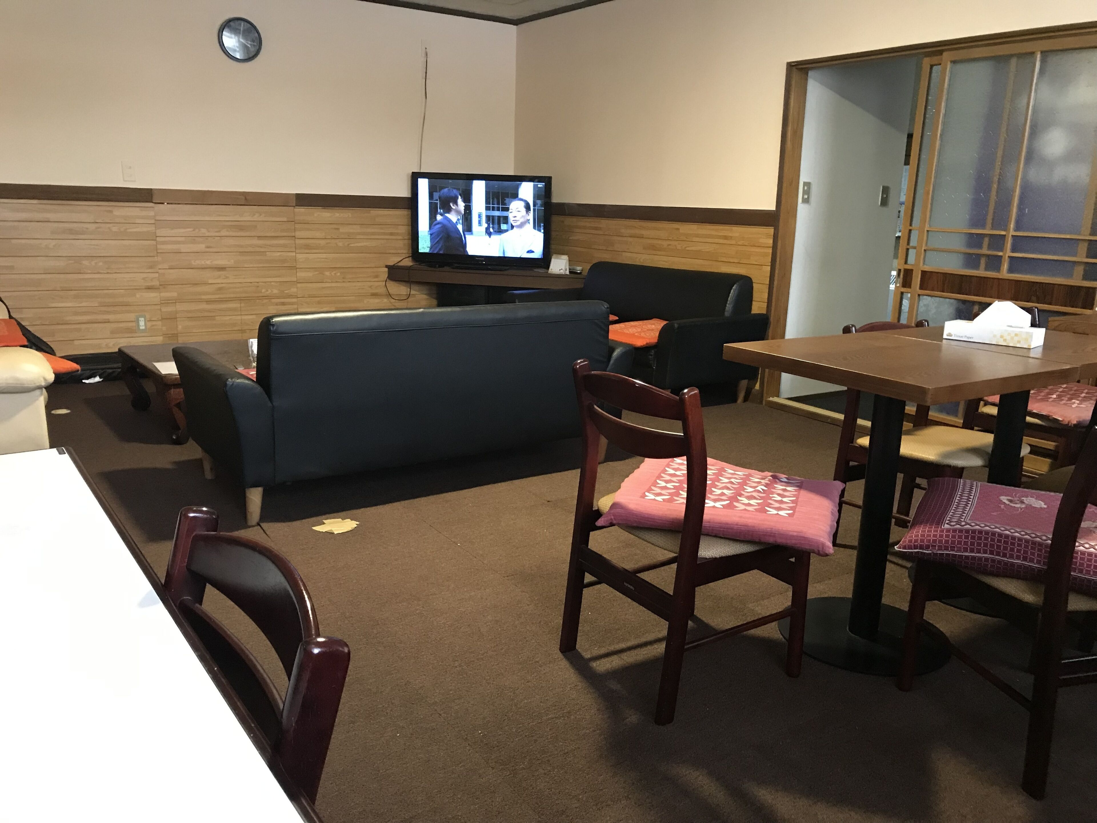 A hotel room with a sofa, a dining table with chairs, a television, and a wooden wall panel.