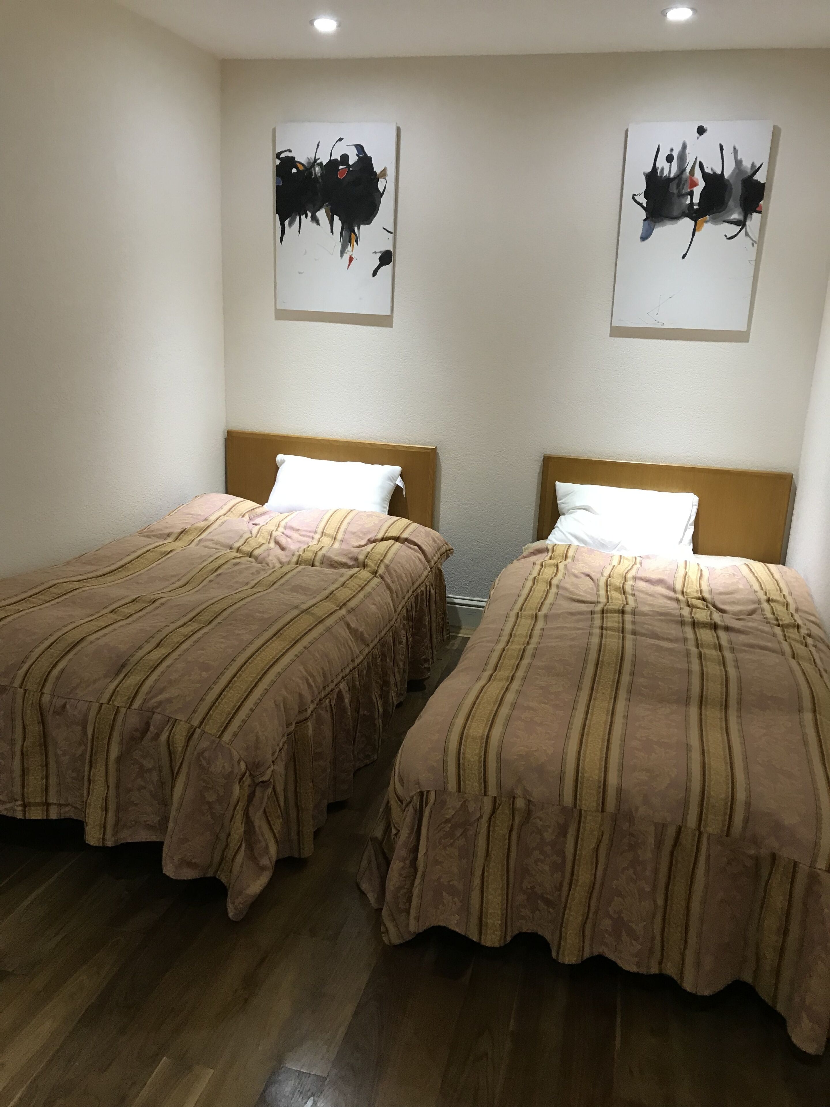Deux lits simples avec des têtes de lit en bois et une literie à rayures, dans une pièce dotée d’un plancher en bois et de murs blancs.