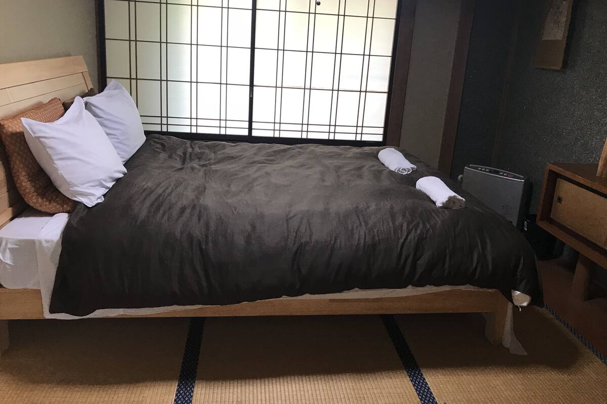 Un lit simple avec un matelas marron foncé et des oreillers blancs, une tête de lit en bois et une fenêtre à carreaux.