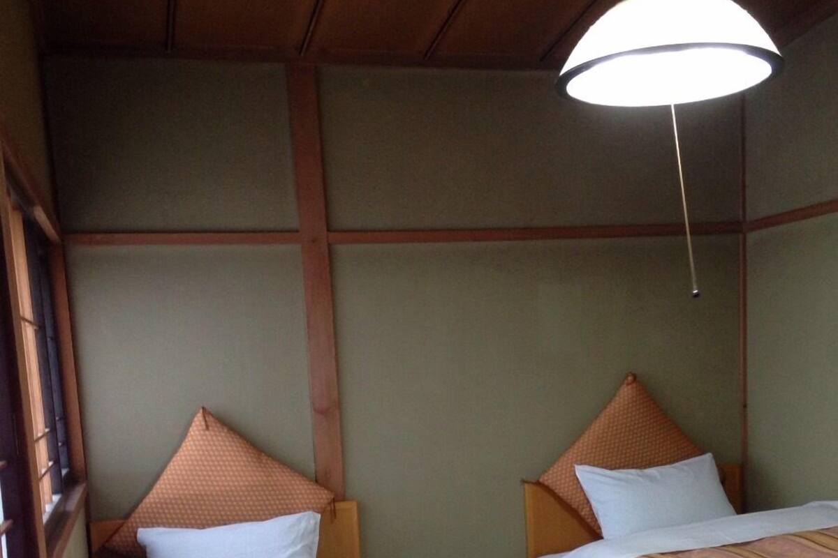 Une chambre avec deux lits, chacun doté d’une tête de lit et d’oreillers, et un luminaire suspendu au plafond.