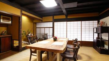 Une pièce de style japonais traditionnel, avec un sol recouvert de tatamis, une table en bois entourée de chaises, un paravent shoji et un plafond bas avec des poutres apparentes.