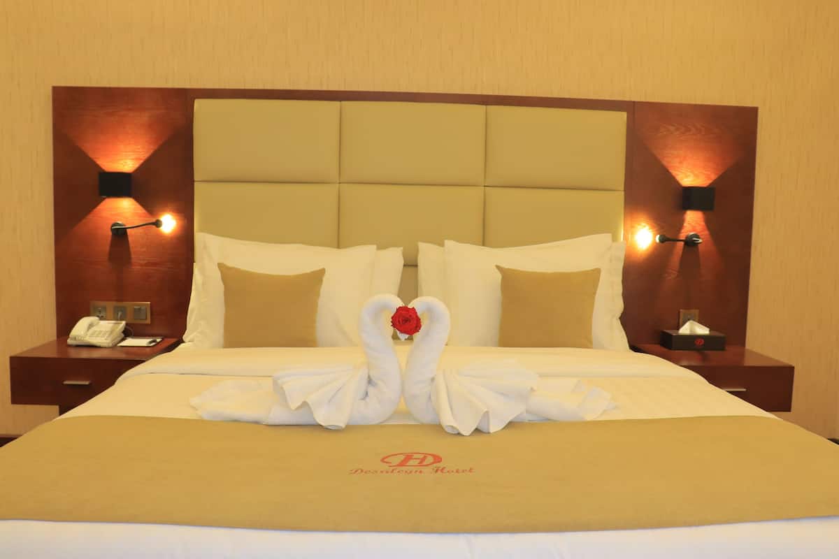 A hotel room with a large bed, two bedside tables, a nightstand, and a headboard with built-in lighting.