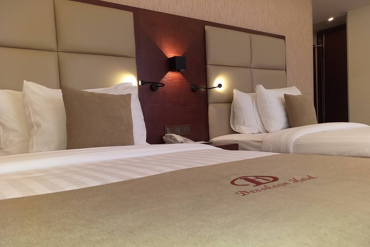 A hotel room with a large bed, a bedside table with a phone, and a wall-mounted light fixture.