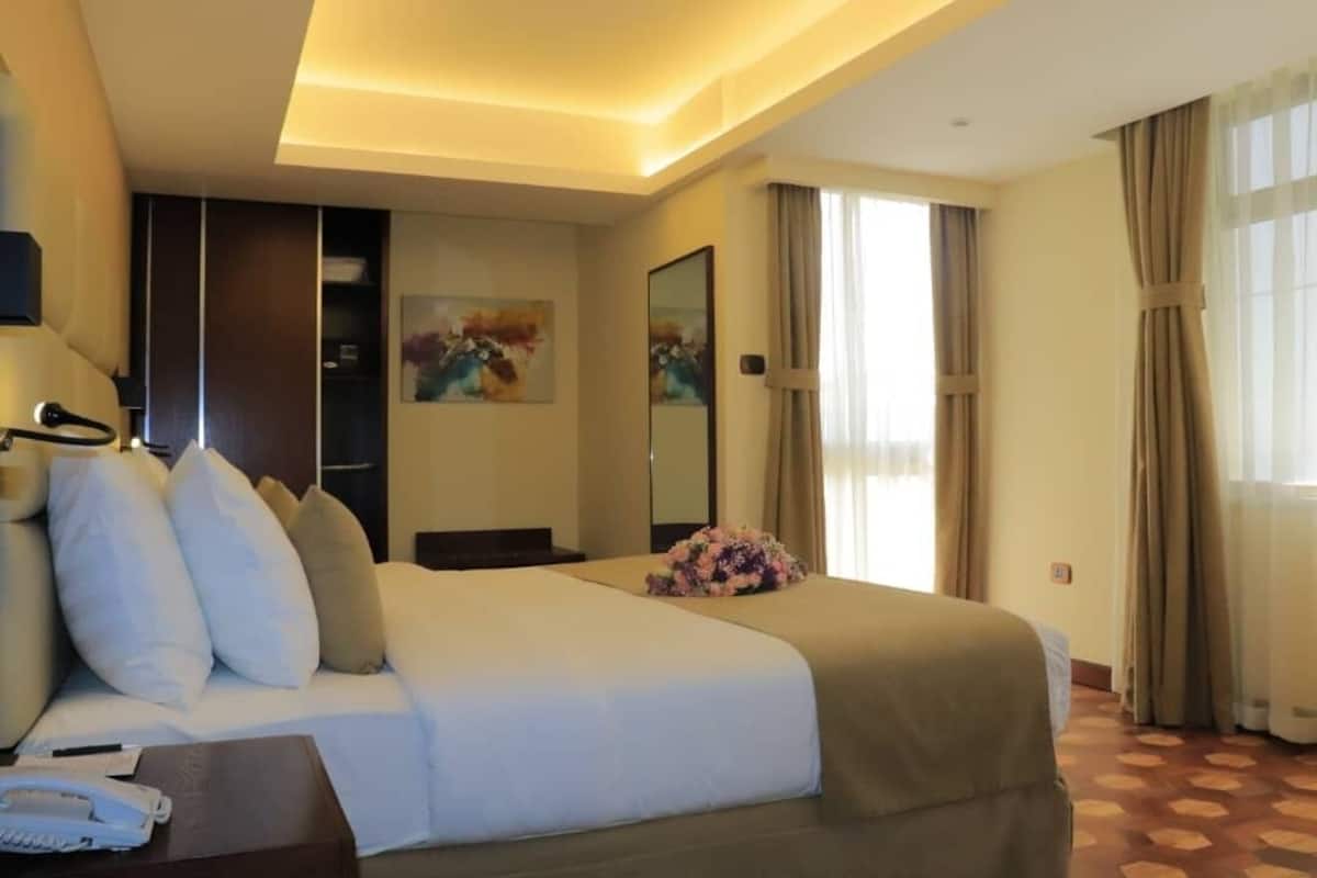 A hotel room with a bed, bedside table, phone, and a floral arrangement.
