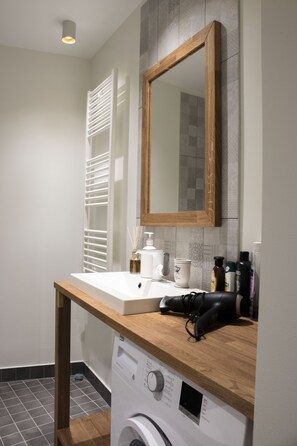 A modern bathroom with a wooden countertop, a built-in washing machine, a mirror, and a towel rack.