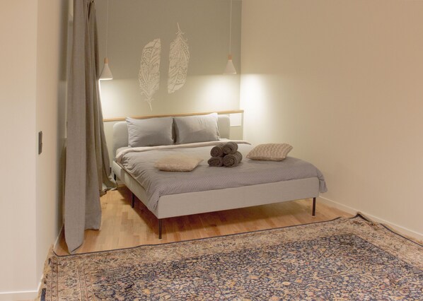 A bedroom with a bed, a patterned rug, and a curtain.