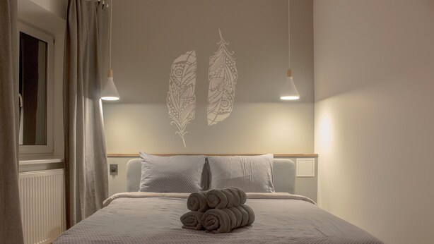 A neatly made bed with rolled towels, a headboard with a leaf pattern, and two pendant lights. - City heart Ülikooli Tartu Home Apts. (Tartu)
