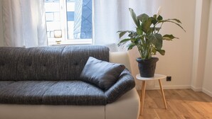 A modern living room with a grey sofa, a small white side table, and a potted plant. - City heart Ülikooli Tartu Home Apts. (Tartu)