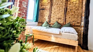 A cozy room with a wooden bed, brick walls, and a small table with a lamp. - Apartment in historischem Gebäude (Uelzen)