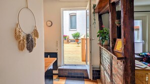 A wooden reception desk with a framed certificate, a potted plant, and a door leading to an outdoor area with a wooden deck and a chair. - Apartment in historischem Gebäude (Uelzen)