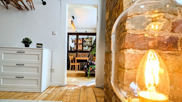 A room with a wooden floor, a white dresser, a green chair, and a brick wall. - Apartment in historischem Gebäude (Uelzen)