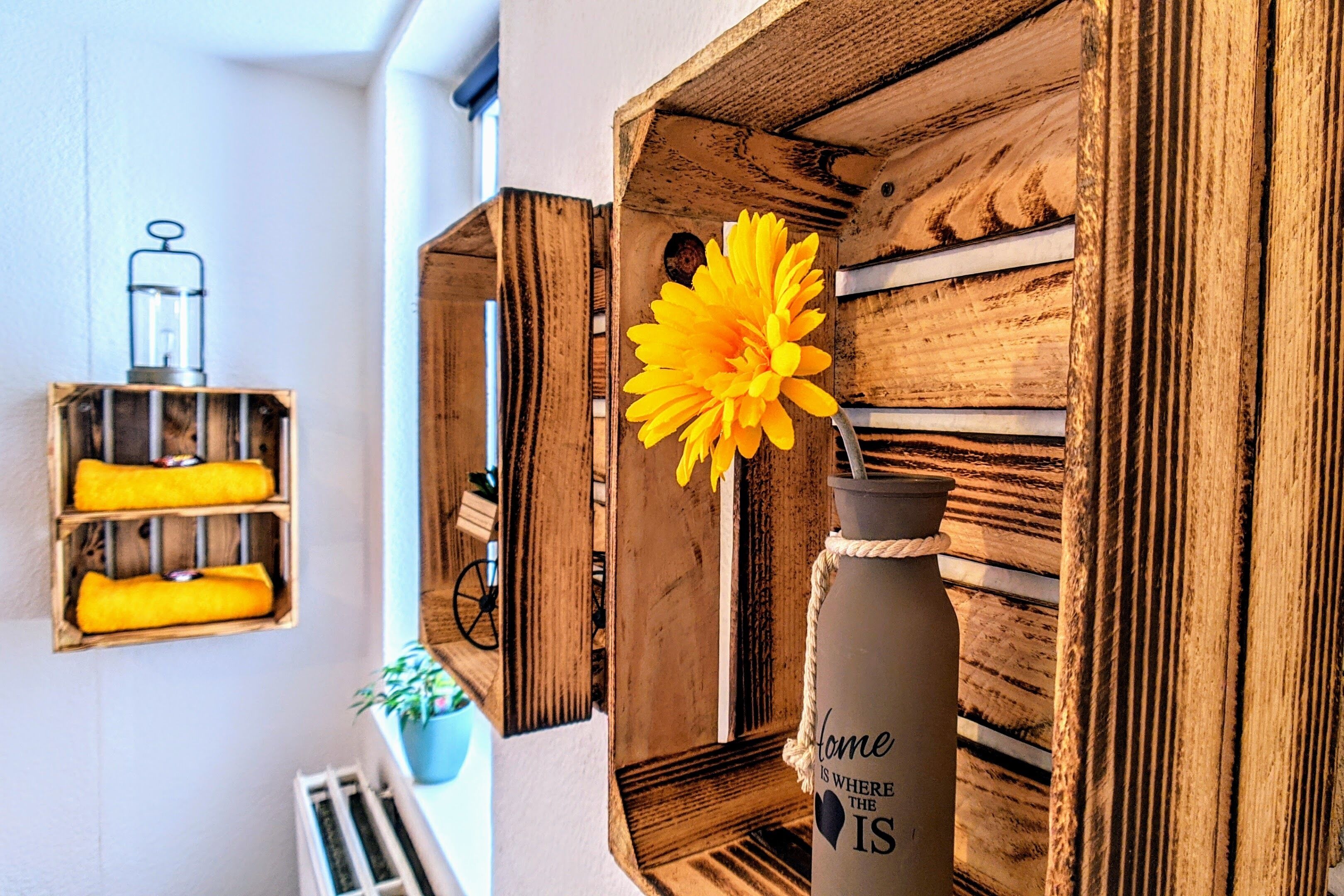 Un estante de madera con una flor amarilla, un recipiente de vidrio y una botella de agua con texto.