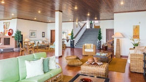 A spacious living area with a green sofa, wicker furniture, a staircase, and a dining area. - FLH Luxury Villa Mar with Private Sea Access (Funchal)