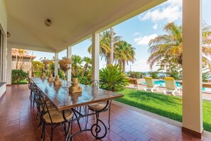A covered outdoor dining area with a long wooden table and chairs, surrounded by potted plants and palm trees. - FLH Luxury Villa Mar with Private Sea Access (Funchal)