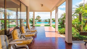 A covered outdoor seating area with chairs and a view of a swimming pool and palm trees. - FLH Luxury Villa Mar with Private Sea Access (Funchal)