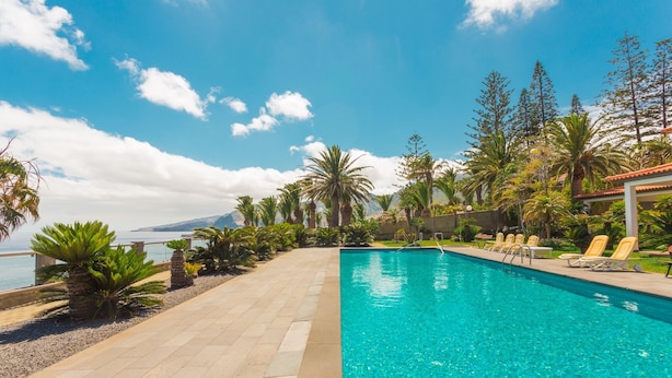 A swimming pool with clear blue water, surrounded by palm trees and a view of the sea. - FLH Luxury Villa Mar with Private Sea Access (Funchal)