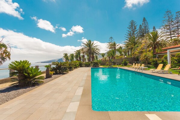 Una piscina con agua cristalina azul, rodeada de palmeras y vista al mar.