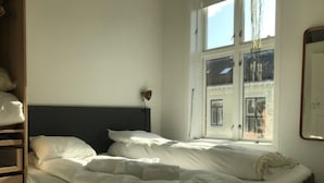 A bed with white bedding, a nightstand, and a window with a view of a building. - StayPlus Apartment near Vigeland Park (Oslo)