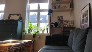 A cozy living room with a large window, a bookshelf, a dark sofa, and a wooden table. - StayPlus Apartment near Vigeland Park (Oslo)