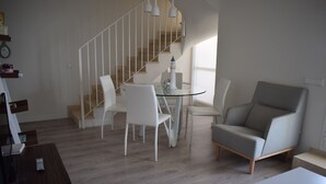 A modern living room with a glass table, white chairs, a grey sofa, and a staircase with white railings. - Anacasa Penthouse Azul Marino Almadrava AT2202 (Denia)