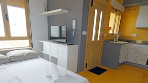 Hotelkamer met een bed, een bureau met televisie, telefoon en een kitchenette met spoelbak en kastjes.