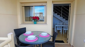 Een glazen tafel met roze tafelonderleggers en witte kommen, zwarte stoelen, een raam met uitzicht, en een trap naar een verdieping erboven.