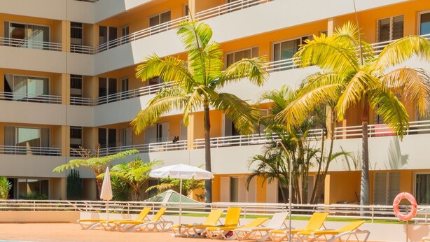 Un hotel de varios pisos con piscina, palmeras y tumbonas.