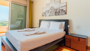 Una habitación de hotel con cama, mesita de noche, lámpara y una obra de arte con vista a la ciudad.