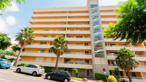 Un hotel de varios pisos con balcones, palmeras y coches aparcados.