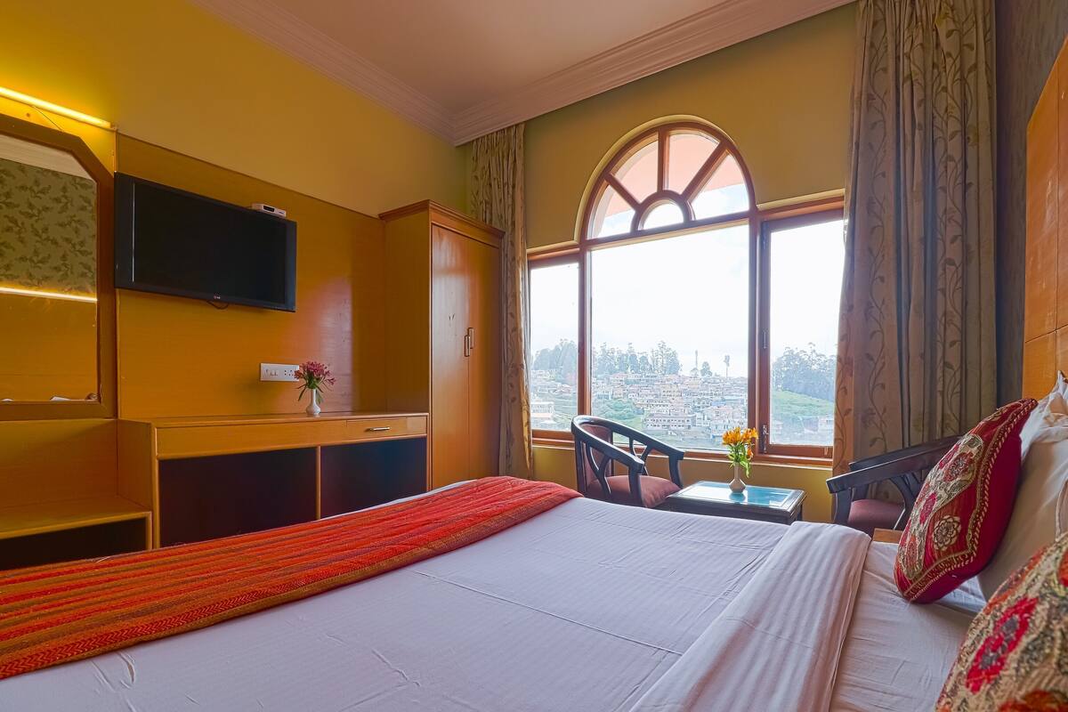 Habitación de hotel con cama, escritorio, silla, televisor y ventana con vistas.