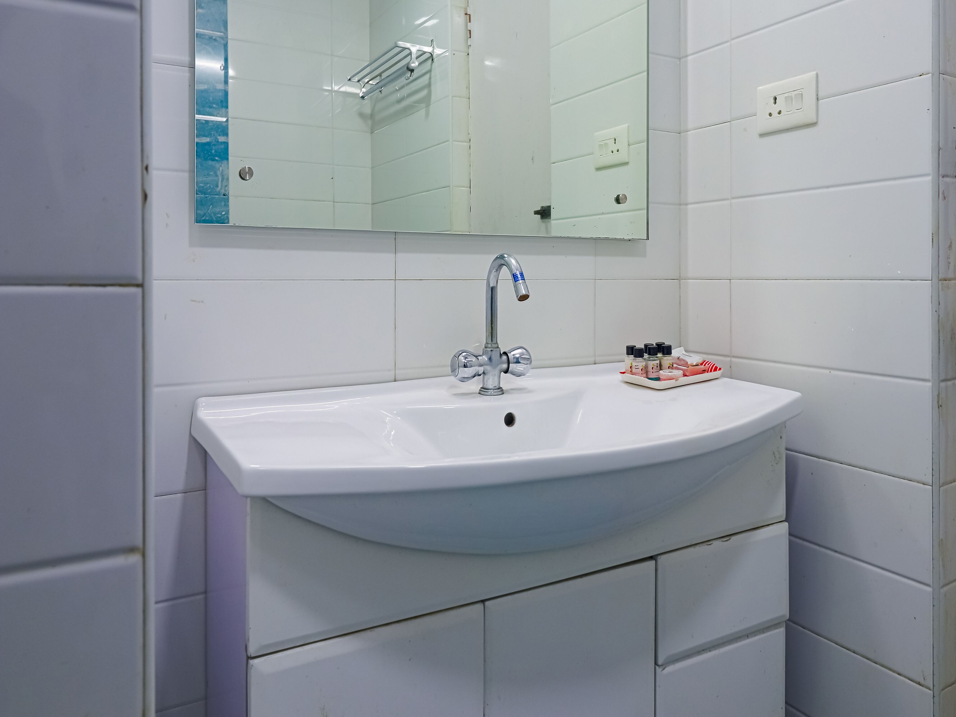 A white bathroom sink with a chrome faucet, a mirror above it, and a tray of toiletries.