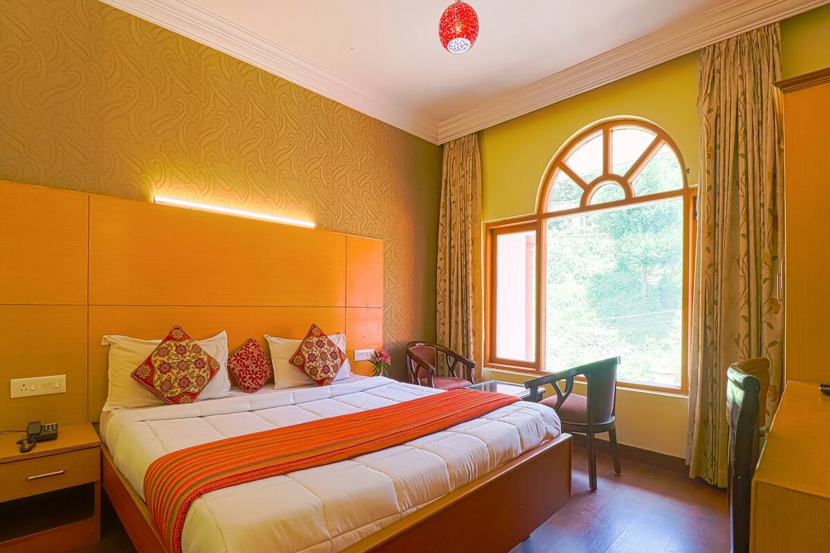 Una habitación de hotel con una cama grande, un escritorio, una silla y una ventana con cortinas.