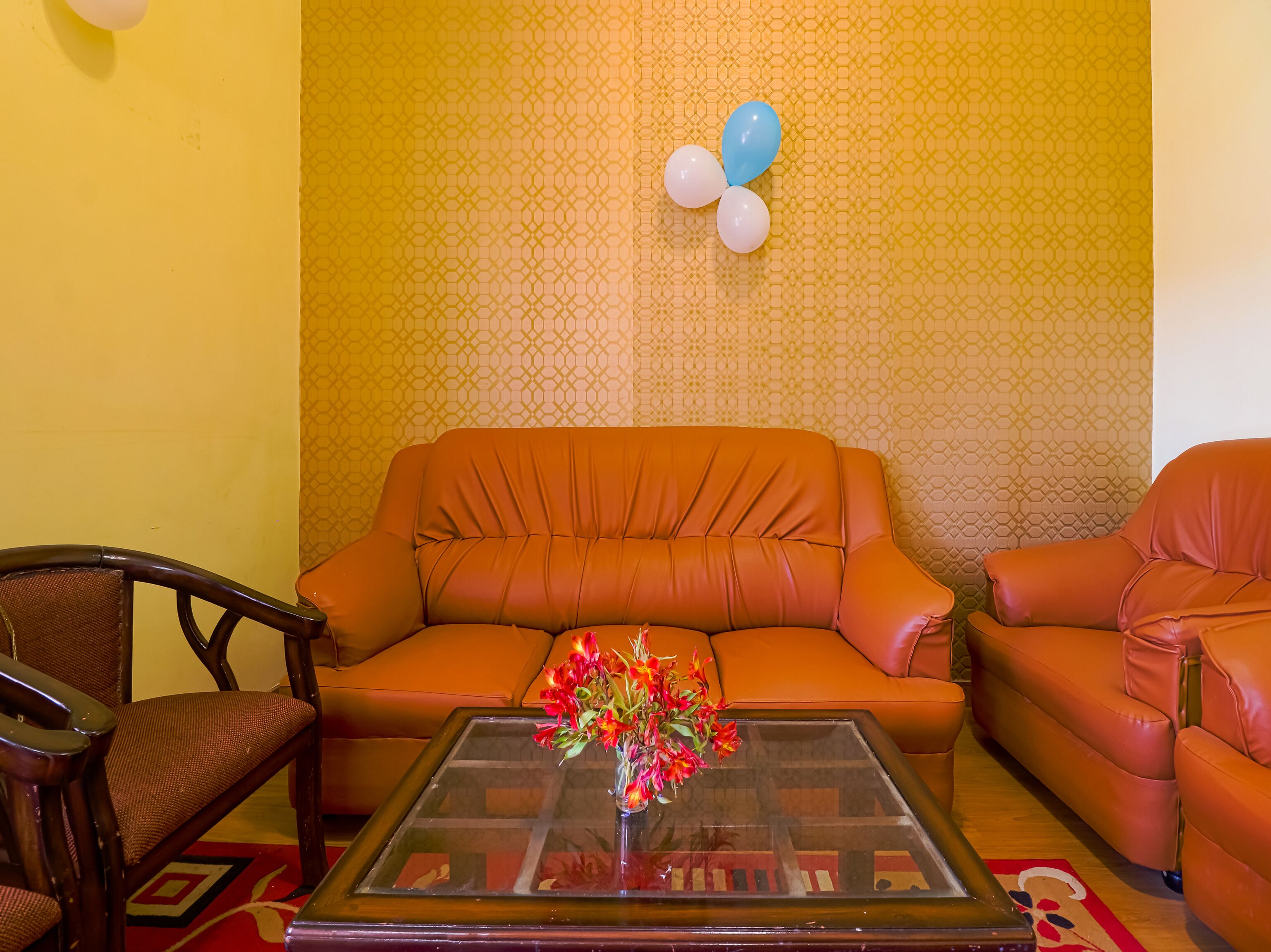 A living room with an orange sofa, a glass coffee table with a floral centerpiece, and patterned wallpaper.