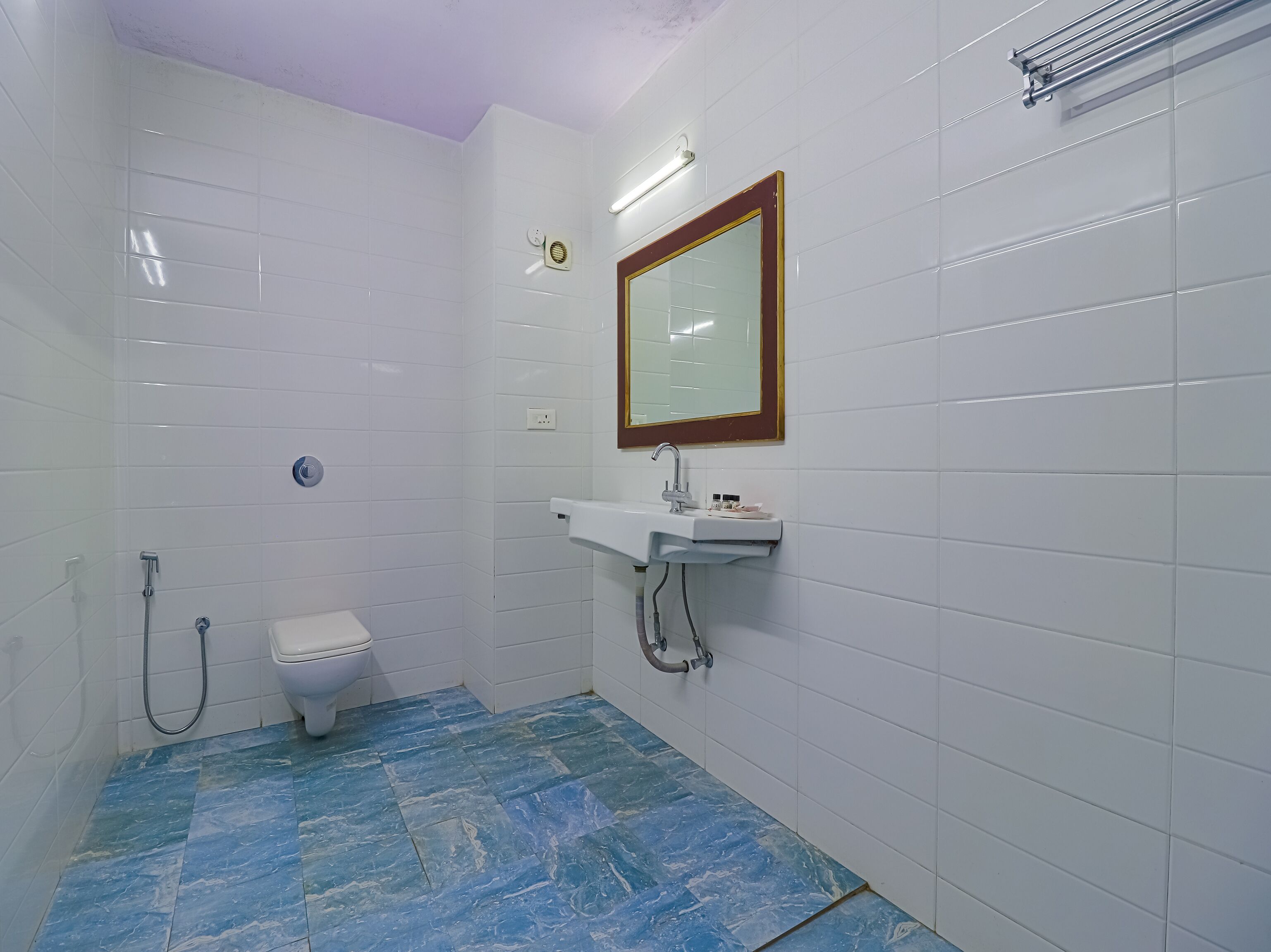 Une salle de bain avec des murs carrelés de carreaux blancs, un sol en marbre, des toilettes, un lavabo avec un miroir et une douche.