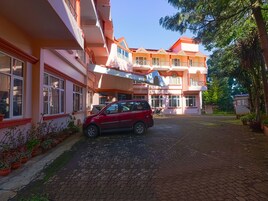 Un coche rojo aparcado frente a un edificio con varios balcones y un camino de entrada pavimentado.