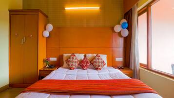 A hotel room with a large bed, a wooden wardrobe, a nightstand with a phone, and a window with a view.
